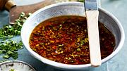 Grillmarinade in einem Schälchen mit Pinsel, im Hintergrund gehackte Kräuter - Foto: House of Food / Bauer Food Experts KG