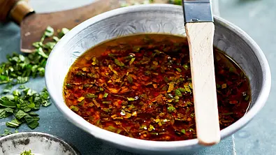 Grillmarinade in einem Schälchen mit Pinsel, im Hintergrund gehackte Kräuter - Foto: LECKER @ Bauer Media Group