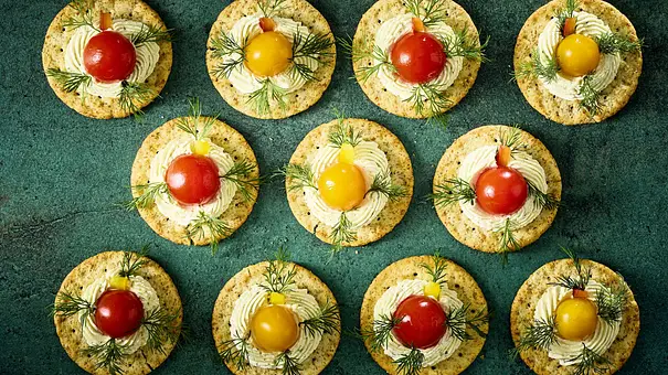Runde Cracker mit einer Cremehaube, garniert mit roten und gelben Kirschtomaten sowie Dill auf einer dunklen Platte angerichtet. - Foto: LECKER @ Bauer Media Group Runde Cracker mit einer Cremehaube, garniert mit roten und gelben Kirschtomaten sowie Dill auf einer dunklen Platte angerichtet. - Foto: LECKER @ Bauer Media Group