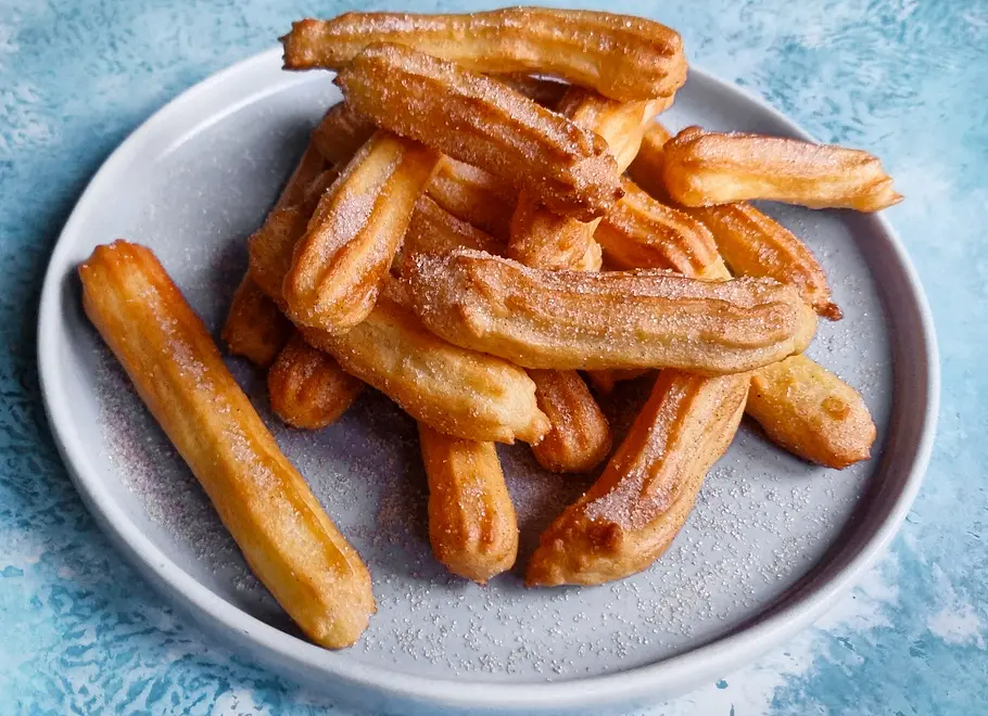 Einige Churros aus der Heißluftfritteuse liegen auf einem Teller, sie sind mit Zimt-Zucker verfeinert.