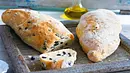 2 Ciabattabrote mit Oliven, ein Brot angwschnitten mit einer Schiebe im Vordergrund. - Foto: LECKER @ Bauer Media Group