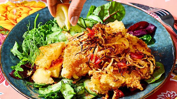 Auf einem blauen Teller sind Cordon-Bleu und Gurkensalat serviert. Eine Hand drückt eine Zitronenspalte darüber aus.  - Foto: House of Food / Bauer Food Experts KG