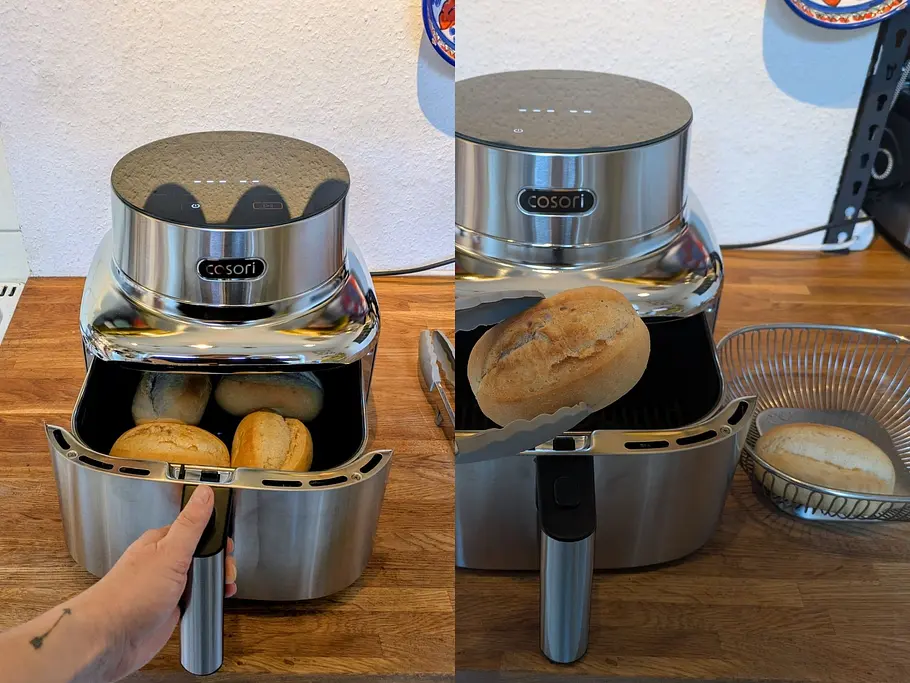 Vier aufgebackene Brötchen liegen in der Cosori- Edelstahl-Heißluftfritteuse, eine Hand nimmt eines mit einer Zange heraus