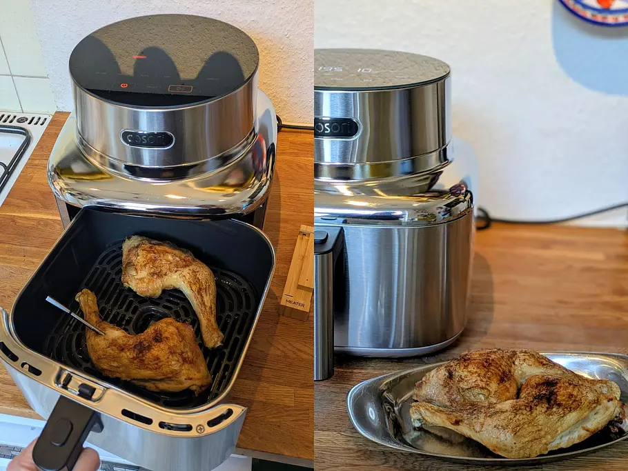Im Garkorb der Cosori Iconic Heißluftfritteuse liegen zwei gebratene Hähnchenschenkel, ein Stück liegt fertig auf einer Edelstahlservierplatte davor.