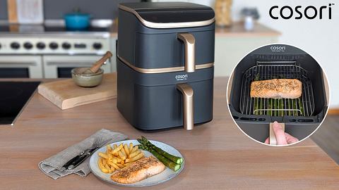 Auf einer Arbeitsplatte steht der Cosori Turbo Tower Pro Airfryer. Davor ein Teller mit darin zubereitetem Lachs samt Pommes und grünem Spargel auf einem Teller. Rechts ein Bild im Bild, das den Lachs zum Ende der Zubereitung im Gerät zeigt, auf einem Rost liegend. Oben rechts in der Bildecke das Logo von Cosori. - Foto: LECKER.de