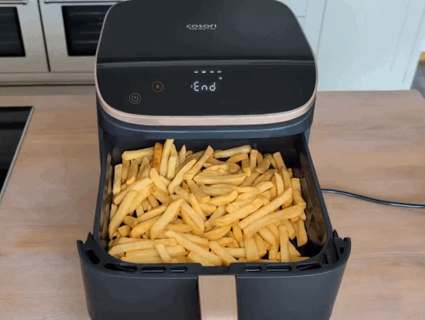 Schubladen auf: eine fertige Mahlzeit aus dem Cosori Turbo Tower Pro Smart Eine Hand öffnet nacheinander beide Schubladen des Cosori Turbo Tower Pro Smart. Auf dem Display oben steht „End“, die Programme sind fertig gelaufen. In der oberen Schublade sind gebackene Pommes zu sehen, unten gebräunte Hähnchenschenkel auf einem Rost.