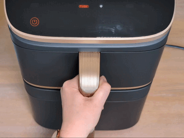 Eine Hand öffnet nacheinander beide Schubladen des Cosori Turbo Tower Pro Smart. In beiden liegen je zwei fertig gebackene Pizzabaguettes, die aus der Vogelperspektive gezeigt werden. Die beiden oberen Baguettes sind deutlich dunkler als die in der unteren Schublade.