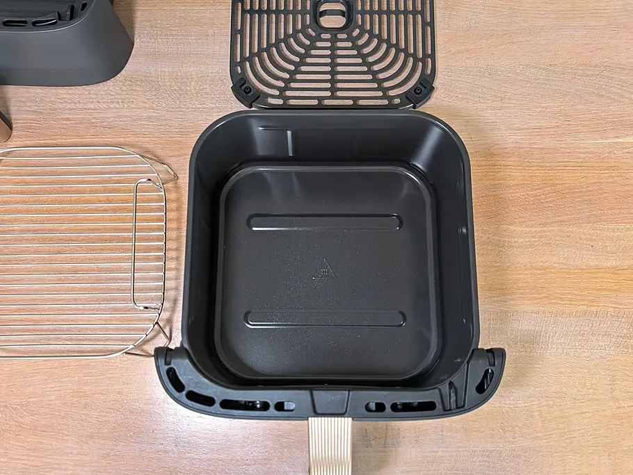 Blick von oben auf eine Arbeitsfläche, auf der eine leere Schublade des Cosori Turbo Tower Pro Smart liegt. Ringsherum liegen die Röstplatte, der Bratrost und die zweite Schublade.
