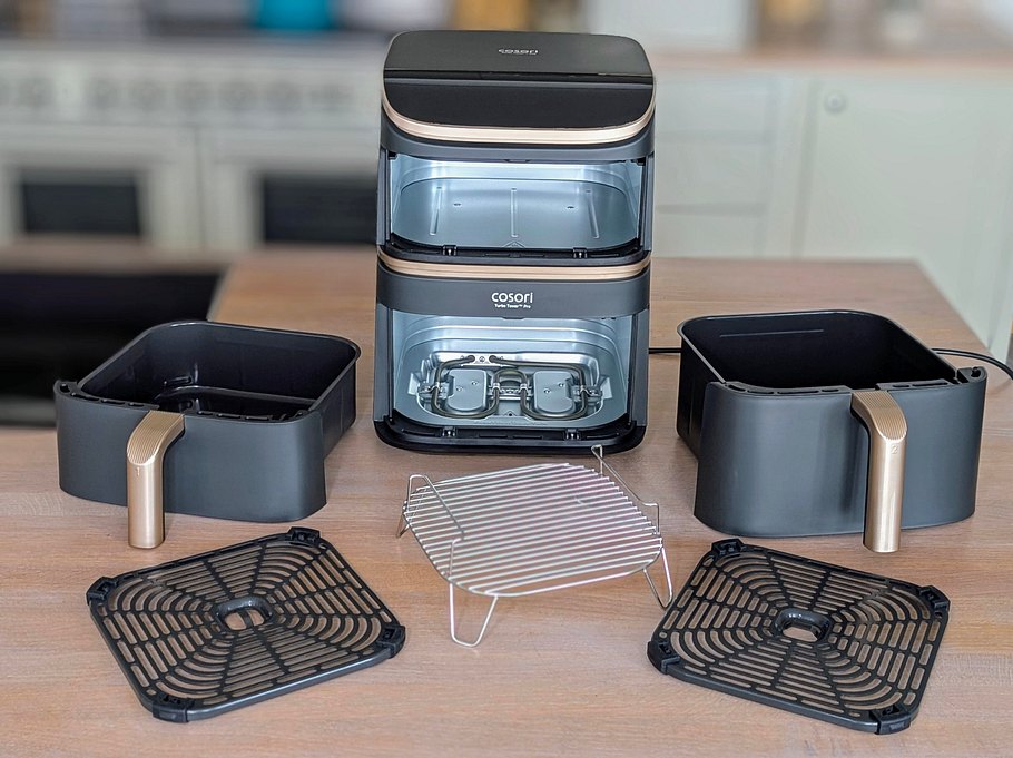 Der Cosori Turbo Tower Pro Smart steht in der Mitte einer Arbeitsfläche. Um ihn herum all seine Zubehörteile: die beiden unterschiedlich hohen Schubladen, zwei Knusperplatten, ein Bratrost.