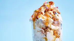 Vanilleeis mit zerbröselten Keksen, Brezeln, Karamellsoße und bunten Streuseln, serviert in einem hohen Eisbecher auf hellblauem Hintergrund. - Foto: LECKER @ Bauer Media Group Vanilleeis mit zerbröselten Keksen, Brezeln, Karamellsoße und bunten Streuseln, serviert in einem hohen Eisbecher auf hellblauem Hintergrund. - Foto: LECKER @ Bauer Media Group