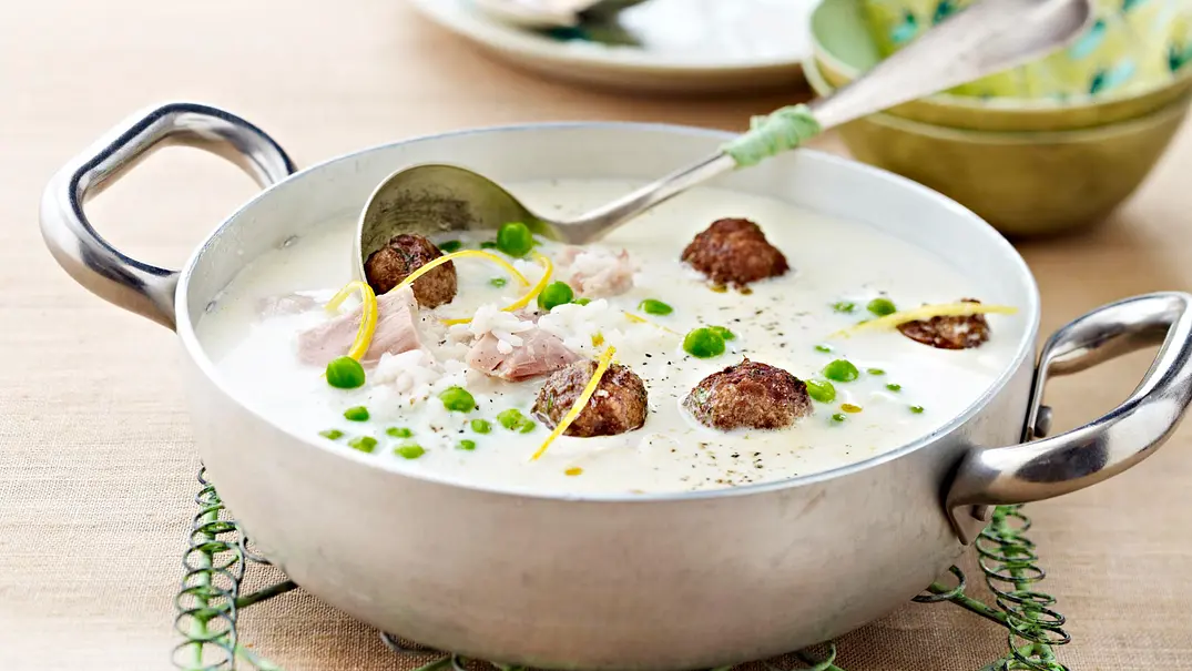 Cremige Hühnersuppe mit Reis und Hackbällchen werden mit Suppenlöffel in einem Kochtopf serviert. - Foto: LECKER @ Bauer Media Group