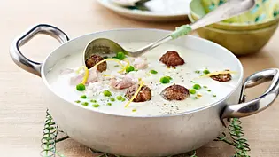 Cremige Hühnersuppe mit Reis und Hackbällchen werden mit Suppenlöffel in einem Kochtopf serviert. - Foto: LECKER @ Bauer Media Group