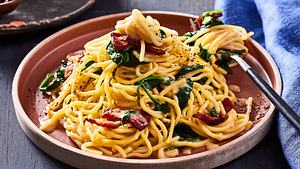 Cremige Miso-Carbonara mit Speck und Babyspinat auf einem terakottafarbenen Teller mit einer Gabel - Foto: House of Food / Bauer Food Experts KG