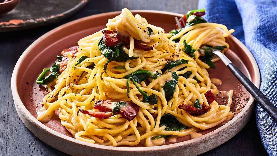 Cremige Miso-Carbonara mit Speck und Babyspinat auf einem terakottafarbenen Teller mit einer Gabel - Foto: House of Food / Bauer Food Experts KG