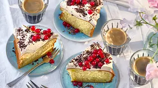 Stücke cremiger Eiscafé-Cheesecake auf hellblauen Tellern, mit Sahne, Schokoraspeln und roten Johannisbeeren garniert, dazu Espressotassen auf weißem Stoff. - Foto: LECKER @ Bauer Media Group