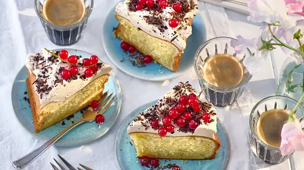 Stücke cremiger Eiscafé-Cheesecake auf hellblauen Tellern, mit Sahne, Schokoraspeln und roten Johannisbeeren garniert, dazu Espressotassen auf weißem Stoff. - Foto: LECKER @ Bauer Media Group