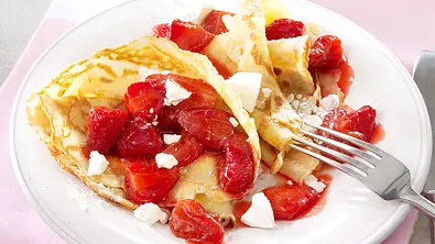 Zwei gefaltete Crêpes mit Erdbeer-Kompott und Baiser-Krümeln auf einem weißen Teller mit angelegter Gabel - Foto: LECKER @ Bauer Media Group