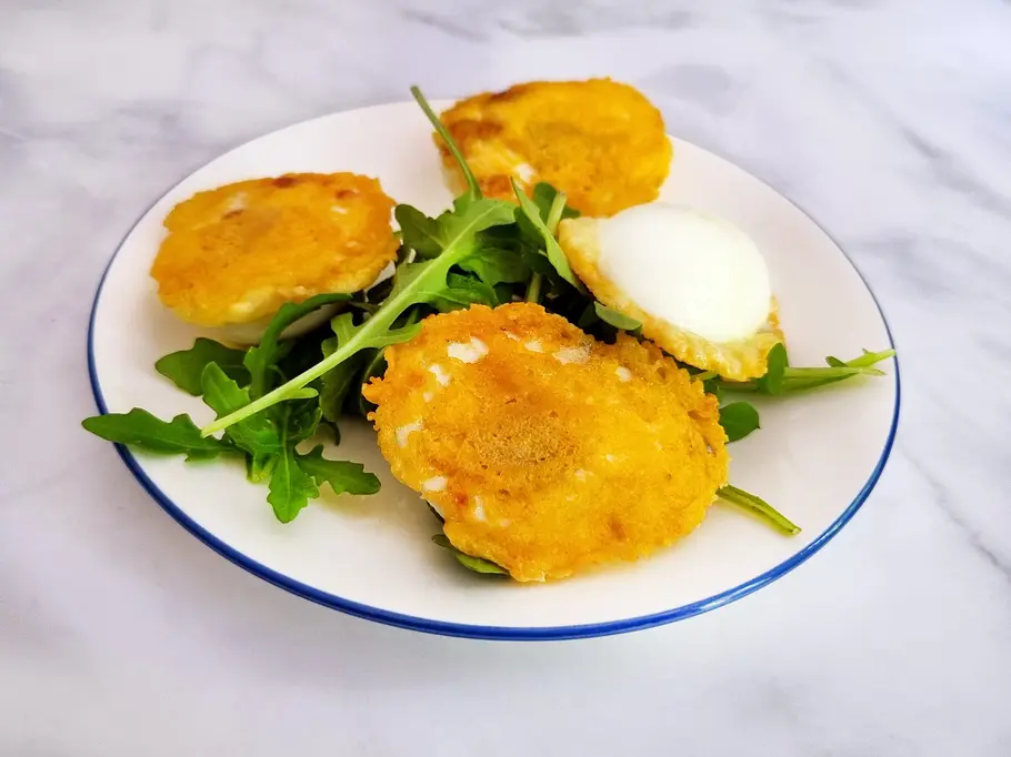 Crispy Eggs mit goldgelber knuspriger Käsekruste auf Rukola.
