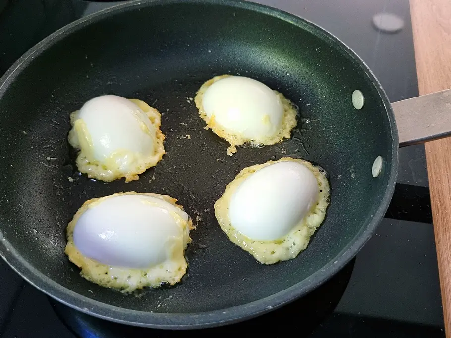 Eier liegen auf Käse in der Pfanne und werden knusprig gebraten.