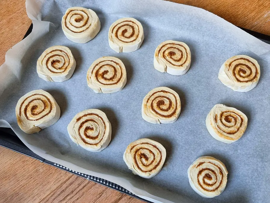 Dänische Zimtschnecken vor dem Backen auf einem Blech Rohe dänische Zimtschnecken liegen auf einem mit Backpapier ausgelegten Blech.