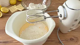 Auf einer hölzernen Küchenarbeitsplatte steht eine weiße Rührschüssel mit Teig, der bemehlt wurde, und darüber sind die Quirle eines cremefarbenen Handmixers sichtbar. - Foto: LECKER @ Bauer Media Group / Nicole Molitor
