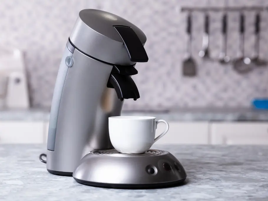 Kaffee Pad Maschine in der Küche Seitenansicht von einer silbernen Senseo-Kaffeepadmaschine mit einer weißen Kaffeetasse auf der Ausgabefläche in einer hellen Küche.