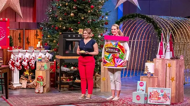 Zwei Frauen stehen in einem weihnachtlich geschmücktem Fernsehstudio und eine steckt in einer menschengroßen Streusel-Packung - Foto: RTL / Bernd-Michael Maurer