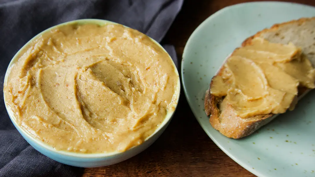 Geröstete Knoblauchbutter in einem Schälchen, daneben liegt eine Scheibe Brot mit Knoblauchbutter auf einem Teller - Foto: Manuela Trinh / LECKER.de