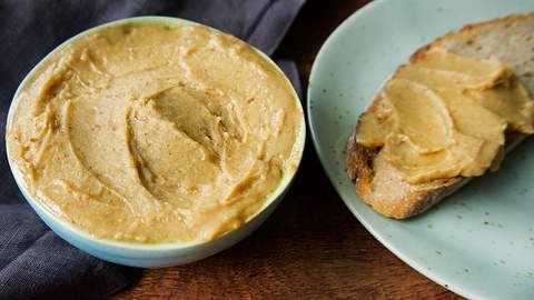 Die geröstete Knoblauchbutter, ein herrlicher Dip zum Grillen) ist goldbraun und bis zum Rand in ein kleines Schälchen gefüllt. Daneben befindet sich ein Teller auf dem ein rustikales Brot liegt, das mit dem Dip bestrichen ist. - Foto: Manuela Trinh / LECKER.de