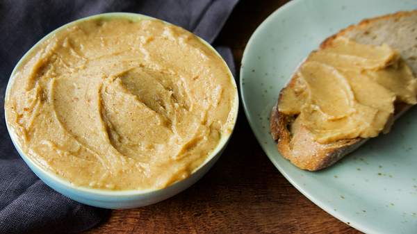 Die geröstete Knoblauchbutter, ein herrlicher Dip zum Grillen) ist goldbraun und bis zum Rand in ein kleines Schälchen gefüllt. Daneben befindet sich ein Teller auf dem ein rustikales Brot liegt, das mit dem Dip bestrichen ist. - Foto: Manuela Trinh / LECKER.de