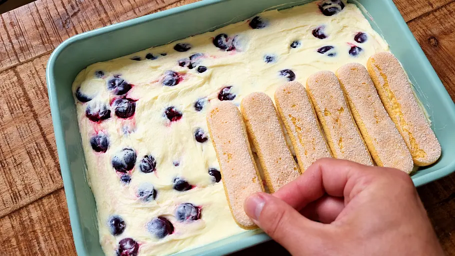 Löffelbiskuits einschichten Die zweite Lage Löffelbiskuits wird auf die Buttercreme mit Kirschen verteilt.