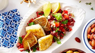 Goldbraun gebratene Doradenfilets auf einem Sommersalat aus gehacktem Gemüse, angerichtet auf einer weißen Fischschale, daneben liegen Zitronenspalten. - Foto: LECKER @ Bauer Media Group