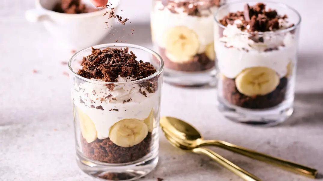 Dreischichtiger Maulwurf-Hügel im Glas mit Schokoladenkuchen, Bananenscheiben und Sahnecreme, getoppt mit Schokoraspeln, daneben goldene Löffel auf heller Oberfläche. - Foto: LECKER @ Bauer Media Group Dreischichtiger Maulwurf-Hügel im Glas mit Schokoladenkuchen, Bananenscheiben und Sahnecreme, getoppt mit Schokoraspeln, daneben goldene Löffel auf heller Oberfläche. - Foto: LECKER @ Bauer Media Group