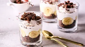 Dreischichtiger Maulwurf-Hügel im Glas mit Schokoladenkuchen, Bananenscheiben und Sahnecreme, getoppt mit Schokoraspeln, daneben goldene Löffel auf heller Oberfläche. - Foto: LECKER @ Bauer Media Group Dreischichtiger Maulwurf-Hügel im Glas mit Schokoladenkuchen, Bananenscheiben und Sahnecreme, getoppt mit Schokoraspeln, daneben goldene Löffel auf heller Oberfläche. - Foto: LECKER @ Bauer Media Group