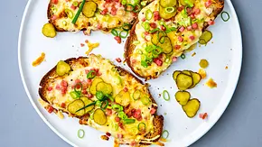 3 Scheiben Flammkuchen-Stulle mit Käse, Schinkenwürfeln und Gewürzgurkenscheiben auf einem weißen Teller - Foto: LECKER @ Bauer Media Group