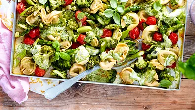 Auf einem Backblech liegen Tortellini mit Brokkoli, grünem Spargel, Kirschtomaten, Basilikum und grüner Sauce. - Foto: LECKER @ Bauer Media Group