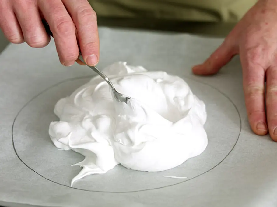 Eischnee wird mit einem Löffel in einen auf Backpapier vorgezeichneten Kreis gestrichen.