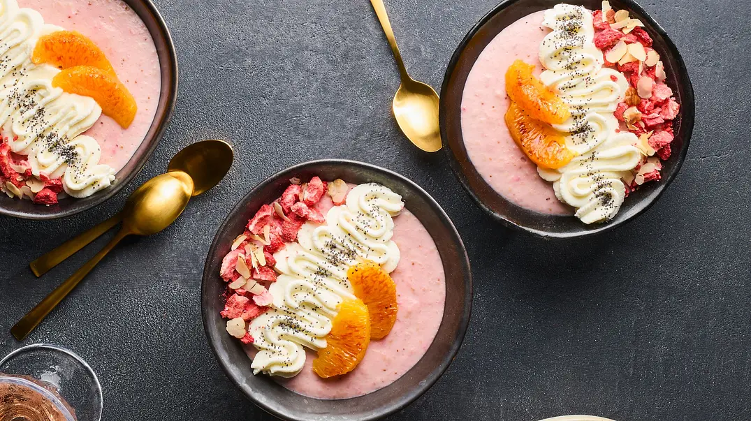 Vier Schüsseln mit cremigem, rosa Erdbeer-Pudding, getoppt mit Blutorangenfilets, Joghurtcreme, gehackten Nüssen und gefriergetrockneten Erdbeerstückchen, serviert auf einem dunklen Untergrund. Daneben ein Teller mit Blutorangenscheiben und Nüssen. - Foto: LECKER @ Bauer Media Group