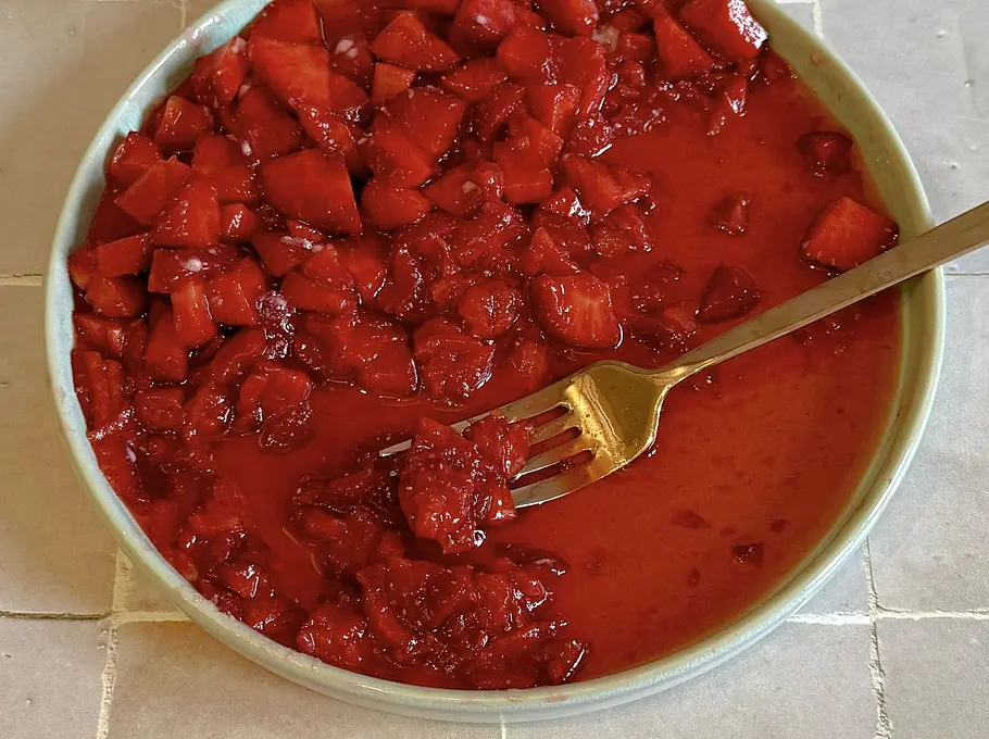 Zerdrückte Erdbeeren in ihrem eigenen Saft und eine Gabel auf einem Teller 