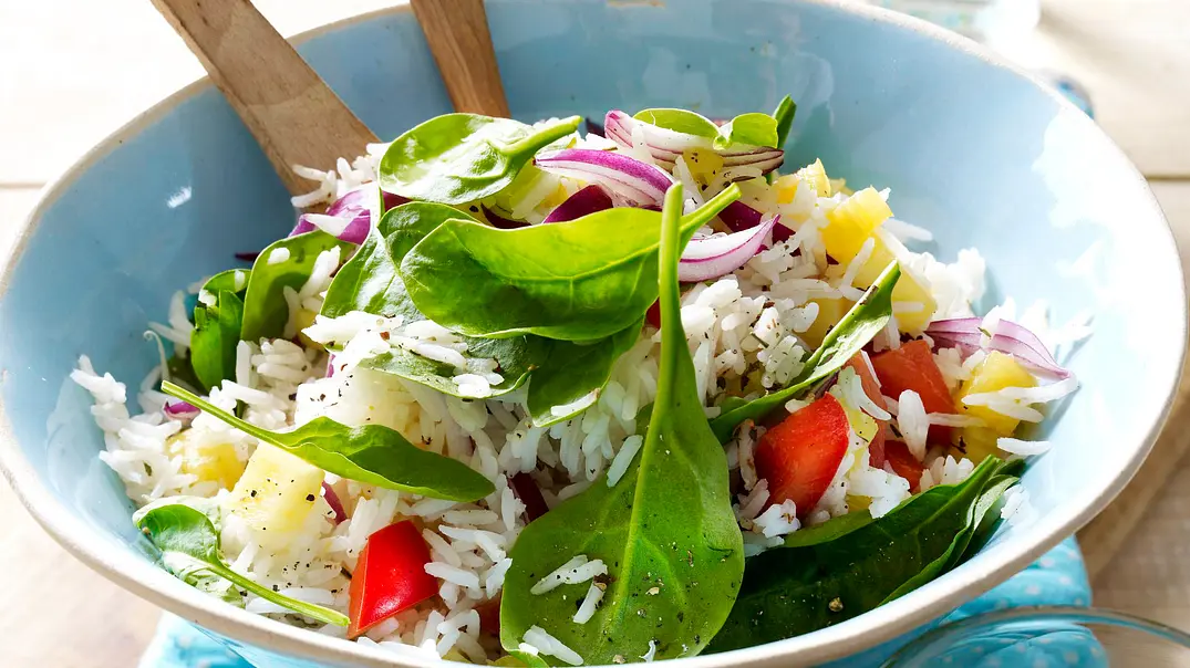 Reissalat mit roter Paprika, Ananaswürfeln und Blattspinat in einer blauen Schüssel mit Salatlöffeln aus Holz. - Foto: LECKER @ Bauer Media Group Reissalat mit roter Paprika, Ananaswürfeln und Blattspinat in einer blauen Schüssel mit Salatlöffeln aus Holz. - Foto: LECKER @ Bauer Media Group