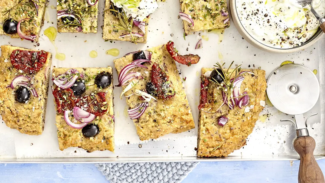In Stücke geschnittene Low-Carb-Focaccia mit Oliven, roten Zwiebeln, getrockneten Tomaten und Rosmarin, auf einem Blech angerichtet, dazu ein Schälchen Dip. - Foto: LECKER @ Bauer Media Group In Stücke geschnittene Low-Carb-Focaccia mit Oliven, roten Zwiebeln, getrockneten Tomaten und Rosmarin, auf einem Blech angerichtet, dazu ein Schälchen Dip. - Foto: LECKER @ Bauer Media Group