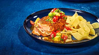 Zartes Cajun-Lachsfilet auf einem dunklen Teller, dazu breite Bandnudeln und Würfel von Tomaten und Avocado als frische Garnitur. - Foto: LECKER @ Bauer Media Group Zartes Cajun-Lachsfilet auf einem dunklen Teller, dazu breite Bandnudeln und Würfel von Tomaten und Avocado als frische Garnitur. - Foto: LECKER @ Bauer Media Group