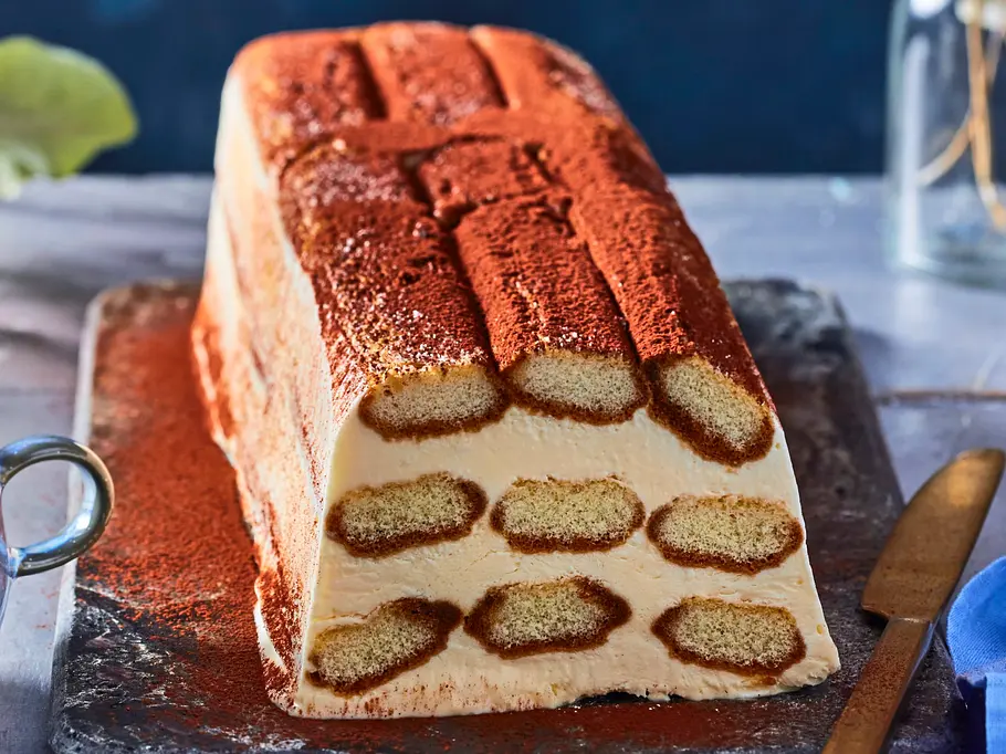 Tiramisu Semifreddo-Style Rezept Tiramisu-Semifreddo in Scheibenform mit Löffelbiskuits und Kakaopulver auf einer dunklen Servierplatte angerichtet.