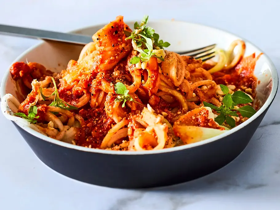 Kohlrabi-Zoodles mit herzhafter Bolognese-Sauce und frischen Kräutern, in einer tiefen Schale serviert und mit etwas Käse bestreut.