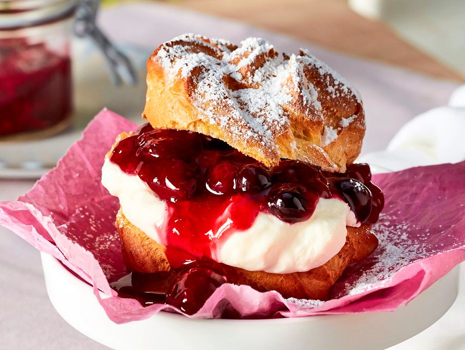 Windbeutel mit sahniger Füllung und fruchtiger Rote Grütze aus Beeren, bestäubt mit Puderzucker.