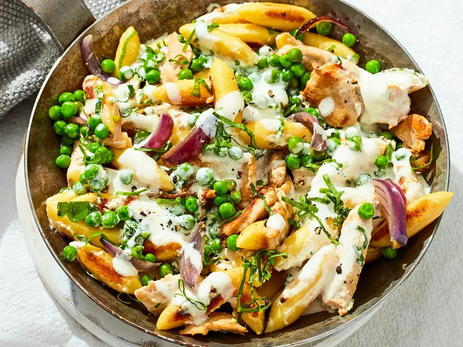 Schnelle Hähnchen-Schupfnudel-Pfanne Rezept Schnelle Hähnchen-Schupfnudel-Pfanne mit goldbraun gebratenen Schupfnudeln, saftigen Hähnchenstücken, grünen Erbsen und roten Zwiebeln, verfeinert mit einer cremigen Sauce, serviert in einer großen Pfanne.