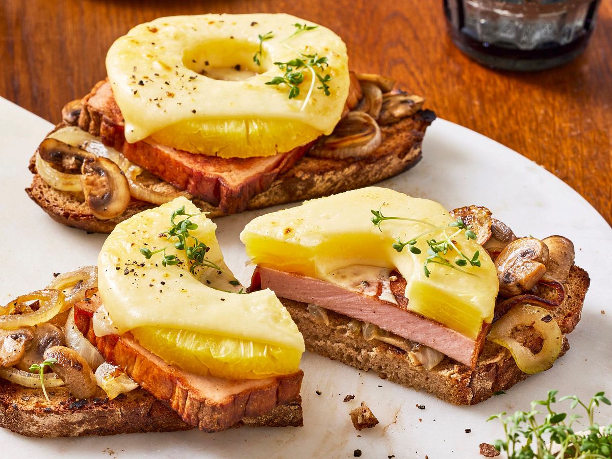 Leberkäse Hawaii mit Ananas und geschmolzenem Käse auf einer Scheibe Bauernbrot, serviert auf rustikalem Untergrund.