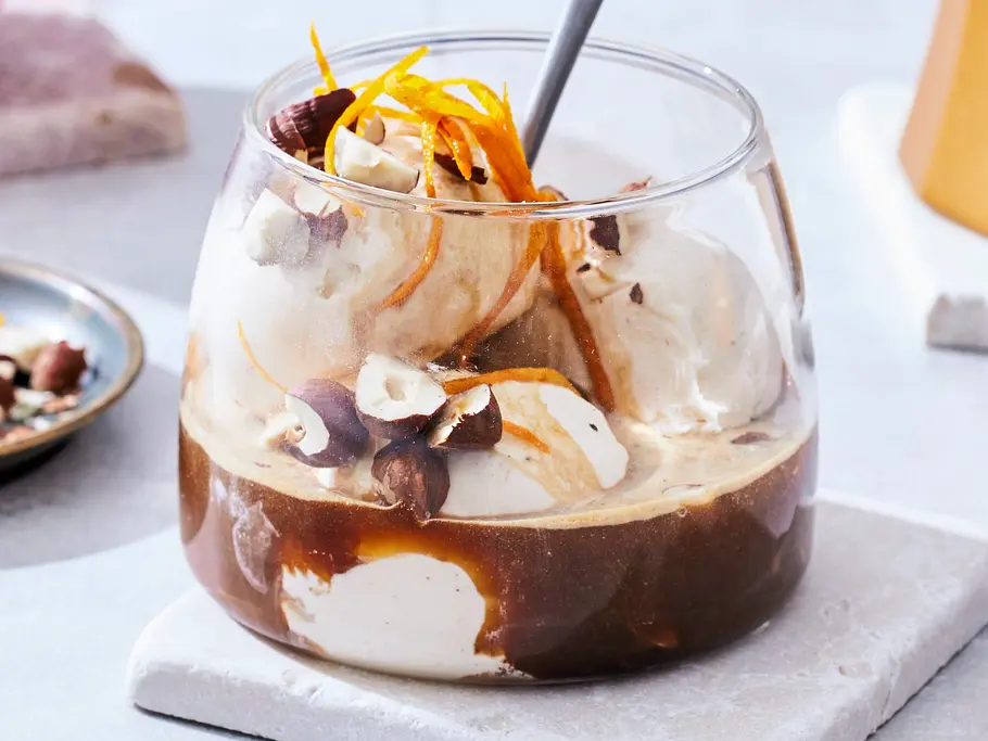 Affogato mit Vanilleeis, Espresso, Orangenzesten und gehackten Nüssen in einem niedrigen Glas auf weißem Untersetzer serviert.