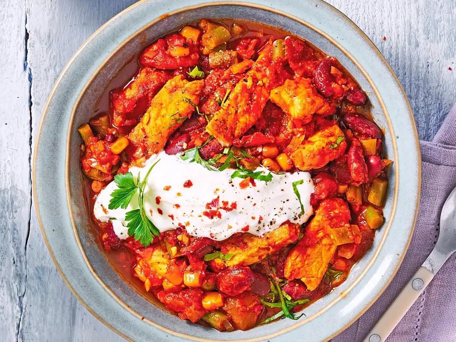 Gyros-Chili One-Pot mit würzigem Gyrosfleisch, Kidneybohnen, Mais und Paprika in einer tomatigen Sauce, serviert in einer Schale mit einem Klecks Joghurt und frischen Kräutern.