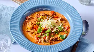 Cremige, orangefarbene Bolognese-Suppe mit Hackfleisch, Gemüse und geriebenem Käse, angerichtet in einem tiefen, blauen Teller auf hellblauer Stoffserviette. - Foto: LECKER @ Bauer Media Group Cremige, orangefarbene Bolognese-Suppe mit Hackfleisch, Gemüse und geriebenem Käse, angerichtet in einem tiefen, blauen Teller auf hellblauer Stoffserviette. - Foto: LECKER @ Bauer Media Group